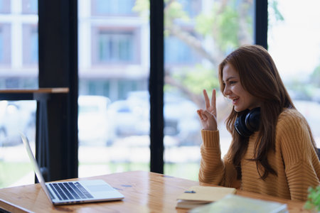 Young woman makes peace sign during a video call on her laptop indoors..の写真素材