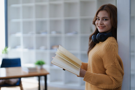 A young woman smiles while holding an open book in a bright modern office..の写真素材