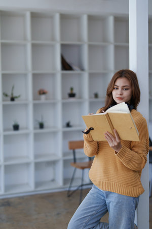 A young woman in casual clothes reads her journal leaning on a white pillar..の写真素材