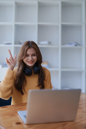 A happy young woman raises her hand during a virtual meeting with laptop.の写真素材