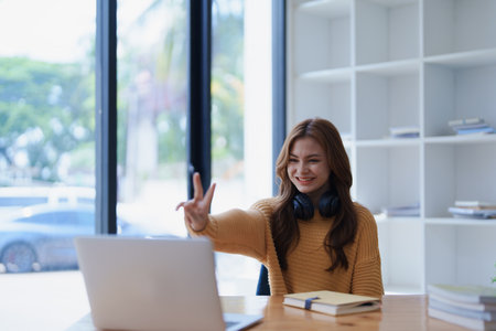 Smiling woman waves during a video conference on her laptop at her desk..の写真素材