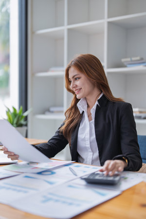 Attractive woman reviews financial documents and calculates figures at desk..の写真素材