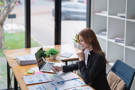 Young businesswoman analyzes charts and graphs at her office desk carefully..の写真素材