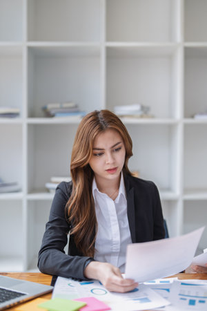 An asian businesswoman reviews paperwork reports at her office workplace..の写真素材