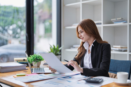 Elegant businesswoman analyzes financial reports at her office desk inside..の写真素材