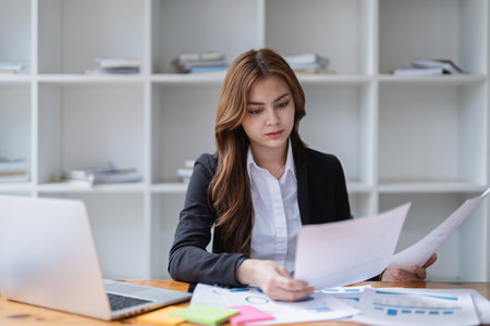 Focused businesswoman analyzes documents at her desk in a bright office space.の写真素材