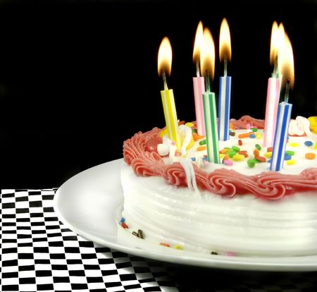 Birthday cake with lit candles on black background.