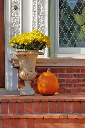 Brick porch with yellow chrysanthemums and a pumpkin in the autumn.の写真素材
