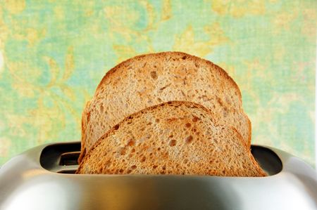 Toasted bread in a stainless steel toaster with a green background.