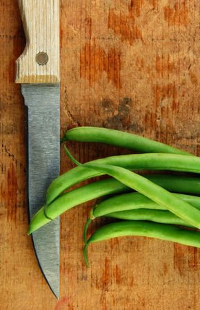 Fresh green beans and a knife on a rustic wooden table.の写真素材