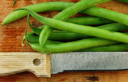 Fresh green beans and a knife on a rustic wooden table.