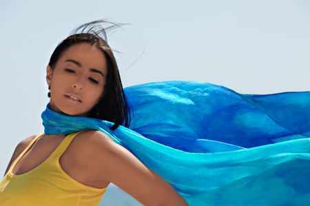 Young Hispanic woman with a blue scarf against a blue sky.の写真素材