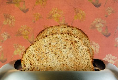Toast in a stainless steel toaster with a pink background.