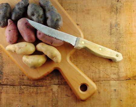 Three colors of fingerling potatoes with a knife on cutting board.の写真素材