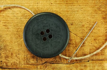 Large button with a needle and twine on a rustic wooden table.の写真素材
