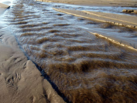 A river swells with water and rushes along a sandy beachの写真素材