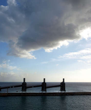 Sun sets through a dark cloudy sky and silhouettes of silos on Barbados dockの写真素材