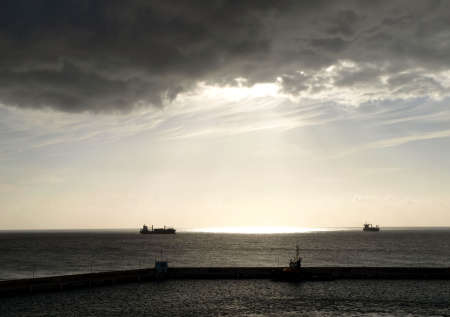 A grey and brooding sky shines sunlight on the ocean and passing freightersの写真素材
