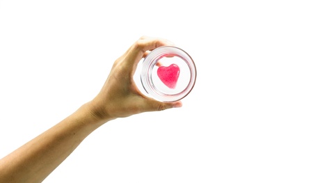 young girl hand hold red heart on small glass isolated on white backgroundの写真素材