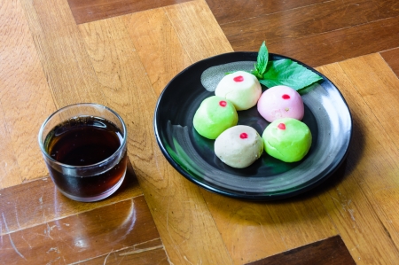 mochi cakes on black dish with black tea in glass on brown wood paquet floor groundの写真素材