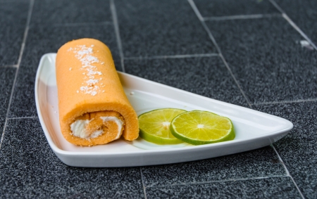 single fruit yellow cake roll with lemon cut on white dish at tile background