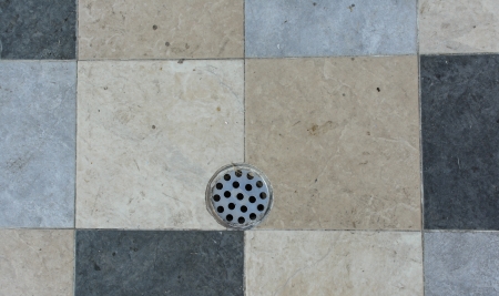 old metal drain hole in the tiled floor cover on public park
