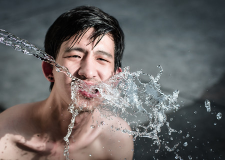 asia man drinking water and splash liquid at summer on outdoor backgroundの写真素材
