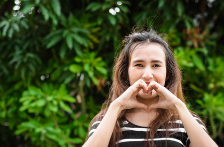Happy asia young woman with make heart love sign by hand in a natural at outdoorの写真素材