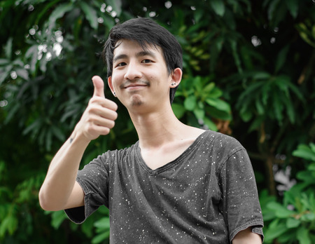 Happy male asia showing thumbs up at outdoor on natural backgroundの写真素材