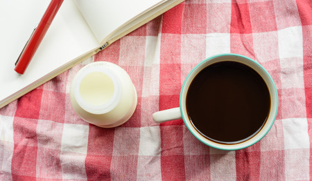 top view Coffee cup and milk bottle on plaid fabric background at outdoor tableの写真素材