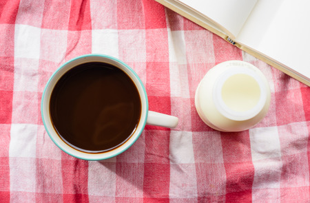 top view Coffee cup and milk bottle on plaid fabric background at outdoor tableの写真素材