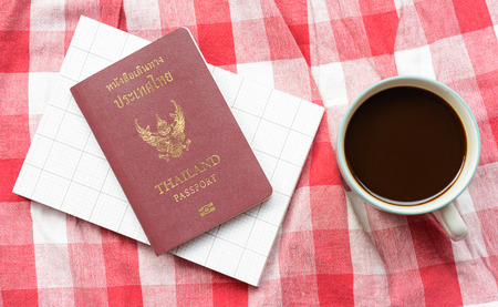 top view Coffee cup and thailand passport book on plaid fabric background at outdoor tableの写真素材