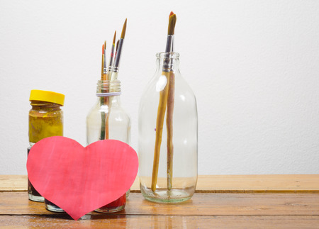 old Brush paints and color bottle with heart paper on wood table at concrete wallの写真素材