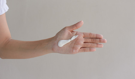 woman hands with skin care cream at wall 