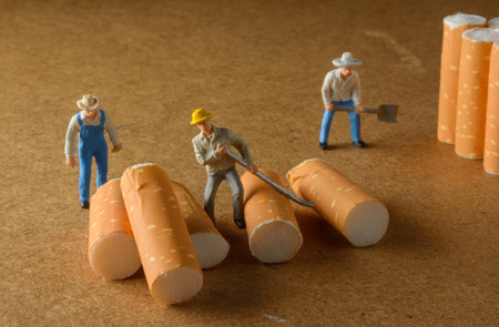 cigarette butt with male miniatures workers on wood pattern with selective focusの写真素材