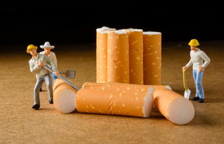 cigarette butt with miniatures workers on wood with selective focusの写真素材
