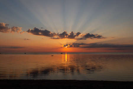 Sun with rays in sky behind clouds during sunrise over sea