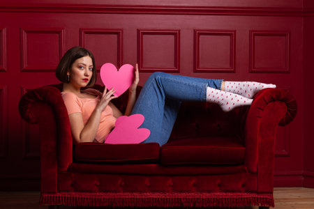 Women in jeans on a couch holding heart-shaped paper sheet in her fingers