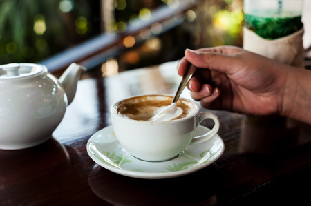 Cup of coffee with hot tea pot on wooden and blur background in over dark tone