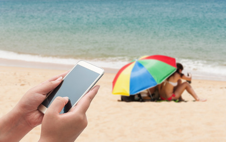 Women using smartphone top on blurred blue sea and white sand beach with some people - Can used for display or montage your productsの写真素材