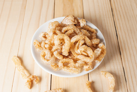 Pork rind junk food snack in white plate on wooden tableの写真素材