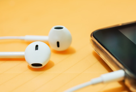 Ear phone into smart phone mobile on blurred orange backgroundの写真素材