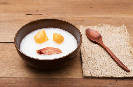Traditional porridge rice gruel or congee in brown bowl with wooden spoon on wood tableの写真素材