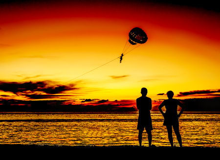 Silhouette lover look at parachute on the sand beach with color of sunset in twilightの写真素材