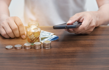 Online banking and mobile banking concept, Saving money and account banking for finance business concept, Man with smartphone and coin money on business office tableの写真素材