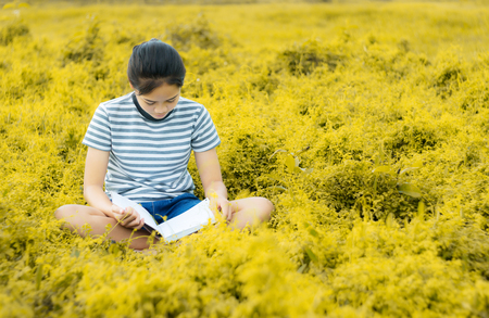 Young girl reading a book in gold meadow contryside nature in evening light vintage styleの写真素材
