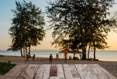 Wooden table top on Sand beach with Someone is playing volleyball on sunset in twilight, Phuket Thailandの写真素材