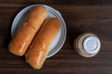 Bread on a white plate sits on a wooden board table with milk in a bottle behind it with copy space. Blurred backgroundの写真素材