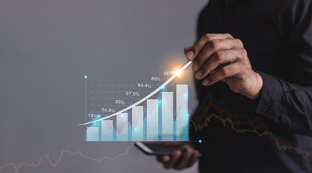 Young man with smartphone mobile hand hold a pen touching to visualize money growth The phone screen displays graphs and charts showing increasing investment and savings trends, along with an increased account balanceの写真素材