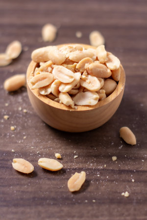 Peanuts in a wooden cup rest on a natural wood floor, creating a warm and rustic food-themed scene,...